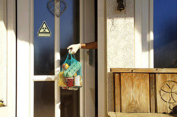 Food delivery. hand of man with medical gloves taking shopping bag at front door, warning sign,...