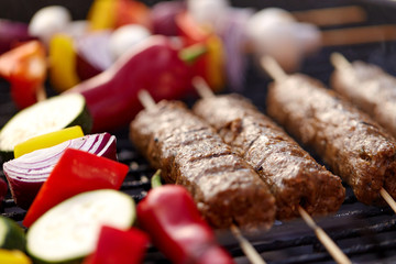 cooking, barbecue and food concept - close up of shish kebab meat and vegetables on bamboo skewers roasting to hot brazier grill outdoors
