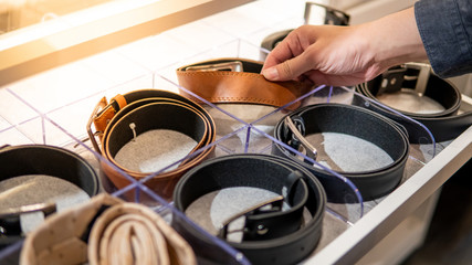 Male hand choosing leather rolled belt from drawer in walk-in closet. Fashion and clothing concept