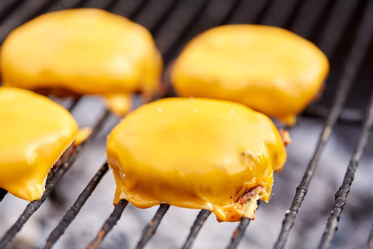 Cooking, Barbecue And Fast Food Concept - Close Up Of Burger Meat Cutlets With Processed Cheese Roasting On Brazier Grill Outdoors