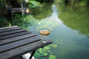 A glass of latte coffee on wooden table with natural lotus lake view
