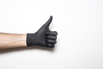 Medical glove in black on a white background. A hand showing the sign of ce well or cool.