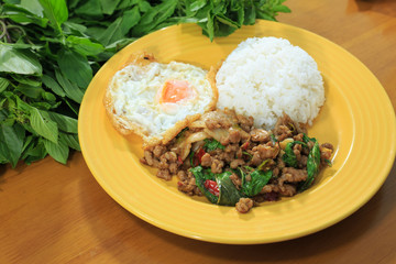 Rice topped with stir-fried pork and basil, fried egg on a yellow plate on a wooden table