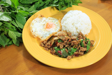Rice topped with stir-fried pork and basil, fried egg on a yellow plate on a wooden table