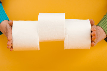 A roll of toilet paper in a woman's hand on a yellow background