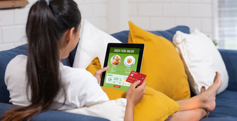 Asian woman order food online with credit card on tablet sitting on sofa at home.digital lifestyle with technology