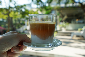 Hand holding a glass of latte coffee