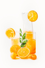 Orange juice in glasses and jug with slices and green leaves at white background. Healthy drinks. Summer beverages. Refreshing. Vitamin C