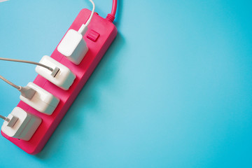 Top view of White mobile charger plugs occupy on pink extension power strip on light blue PVC...