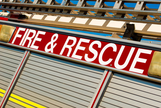 Angled view of FIRE & RESCUE sign on the side of a British ladder and pump fire engine, against a clear blue sky.
