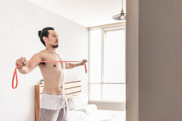 Asian man stretching his muscle in concept of workout at home with resistance band.