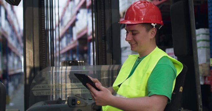 Happy engineer typing on tablet during work in telescopic forklift