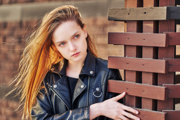 Girl teenager with long hair posing near a wooden fence.