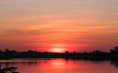 A quiet freshwater lake is reflection of the sun on water surface. Silhouetted the trees along the coast. During the sunset.