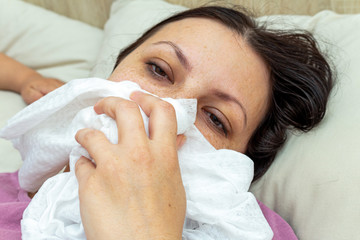 sick woman suffers from viral flu in bed, blows his nose in a disposable handkerchief