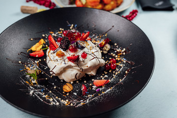 Pavlova cakes with fresh raspberries and blueberries on dark plate in restaurant