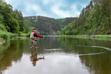 Fototapeta na wymiar Caucasian elderly fisherman with fishing rod in river water. Hunting and hobby sport