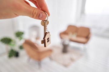 Men hand holding key with house shaped keychain. Modern light lobby interior. Mortgage concept....