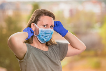 Coronavirus outdoor portrait, blonde woman putting on a protective mask looking at the camera. COVID-19 concept. Selective focus with copyspace.