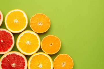 Citruses fruits on green background with copyspace, fruit flatlay, summer minimal compositon with grapefruit, lemon, mandarin and orange
