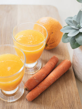 Zwei Gl&auml;ser Orangensaft mit einer Orange, Karotten und eine Pflanze auf Holztisch