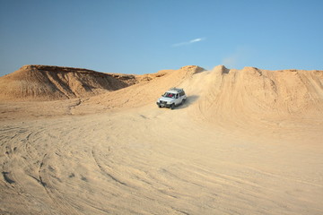 Fototapeta na wymiar Sahara desert, Tunisia. August 2012. White touristic jeep in dunes of the Sahara. Tourism, travel on car, adventure. North Africa