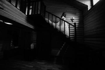 Beautiful bride in a white dress with long train is climbs up the stairs in a classic interior.