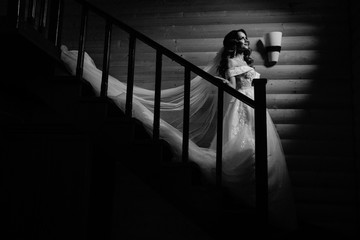 Beautiful bride in a white dress with long train is climbs up the stairs in a classic interior.