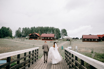 Newlyweds are walking in the park, the bride is holding a wedding bouquet in her hands, they are standing with their backs © olegzaicev