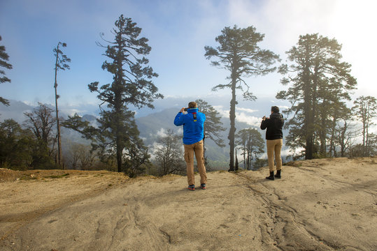 Couple photographing at Dochula looking across forests to  Himalayan peaks Bhutan