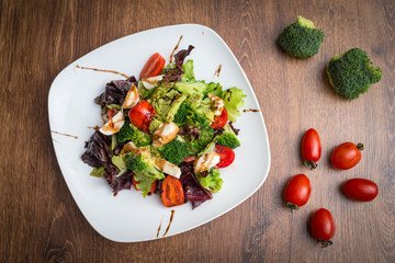 Vegetable salad with mozzarella, tomatoes, broccoli and basil in a plate on a wooden background Top view.