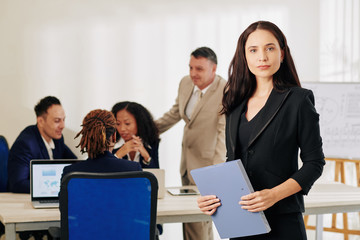 Beautiful confident young businesswoman with documents folder looking at camera