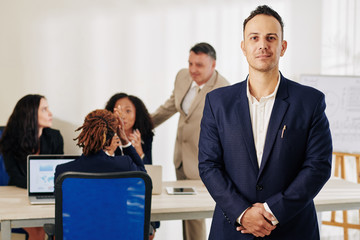 Portrait of young confident businessman standing in meeting room and looking at camera