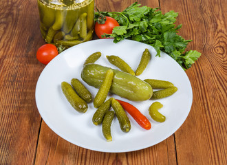 Pickled ordinary cucumber and gherkins on saucer against other vegetables