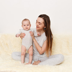 a smiling Caucasian woman hugs an eight-month-old baby girl at home.