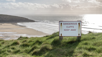 A sweeping beach on the South Wales coast, UK on a bright, winters day. There is a sign that says "Dangerous Cliffs, keep away"