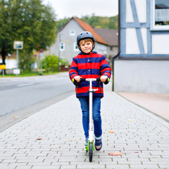 cute little school kid boy with helmet riding on scooter in park nature. children activities outdoor in winter, spring or autumn. funny happy child in colorful fashion clothes. © Irina Schmidt