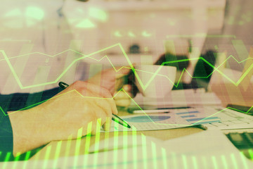 Double exposure of man's hands writing notes of stock market with forex graph.