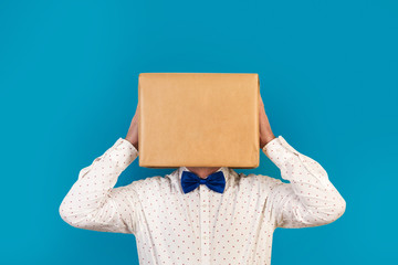 Hombre con caja de cartón en la cabeza con gesto pensativo con manos sostenien sobre fondo azul clásico. Vista de frente. Copy space - obrazy, fototapety, plakaty