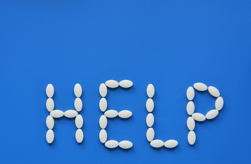 Request for help during illness. A pandemic virus around the world. Pills closeup on a blue background. Vitamins in the form of a word.