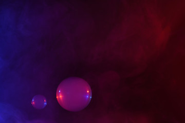 Two soap bubbles filled with smoke flowing over abstract colorful clouds of vapor with copy-space.