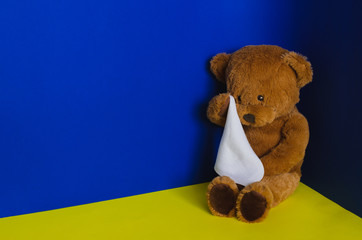 Teddy bear doll sitting at the corner and crying with handkerchief. Child abuse concept.