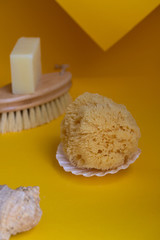 Natural sea sponge on the sea shell, bamboo clean brush and natural soap bar on yellow background. Eco sustainable living and no plastic concept.