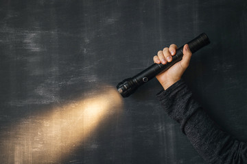 A flashlight in a man’s hand and a ray of light in the dark on a black background. Modern LED lamp with bright projection. Surface with copy.