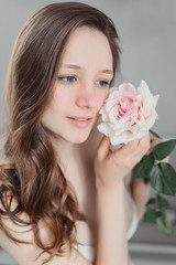Obraz na płótnie Canvas A young brunette girl with cumbersome hair without makeup holds a pink rose. Flower about the person. Natural beauty and naturality.
