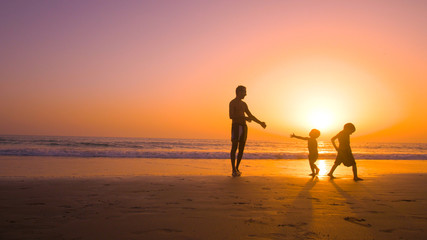 Father with kids playing in the beach at sunset