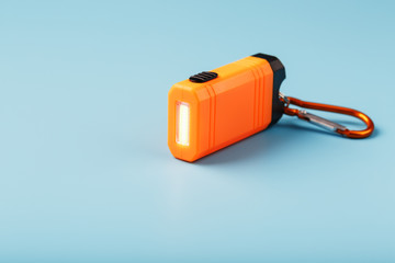 An orange led flashlight with a carabiner glows on a blue background.