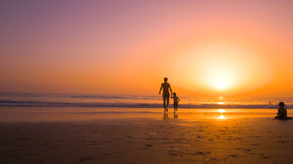 Father with kids playing in the beach at sunset