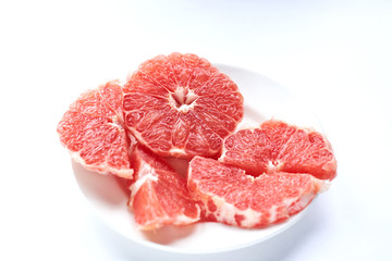 sliced ​​red grapefruit on a white plate on a white background