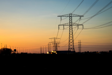 Fototapeta premium High-voltage pylons with power lines for the transport of electricity are outlined against the twilight sky